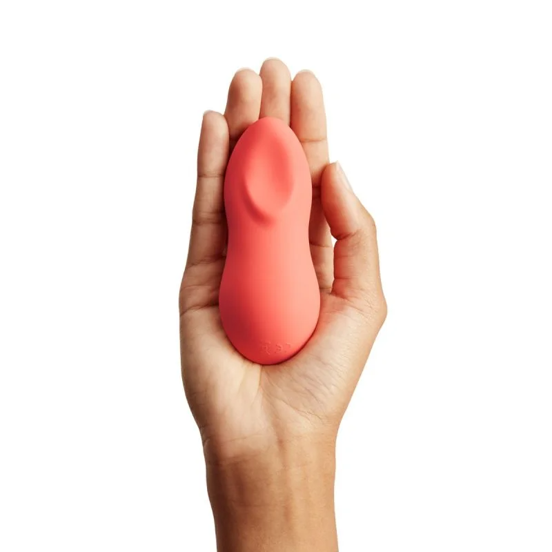 A coral-colored vibrating massager held in a hand.