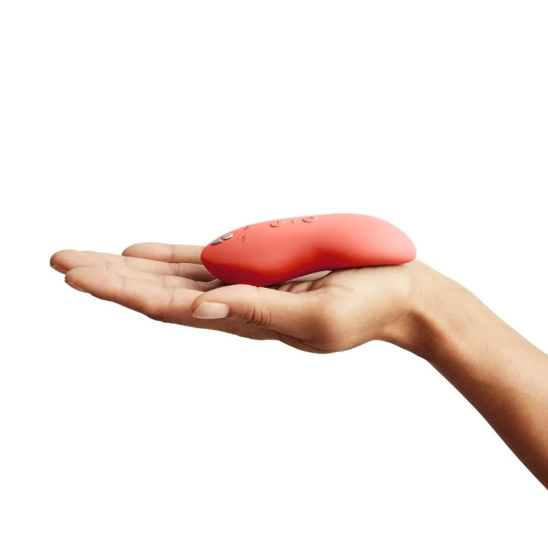 A coral-colored vibrating massager rests on an open palm.