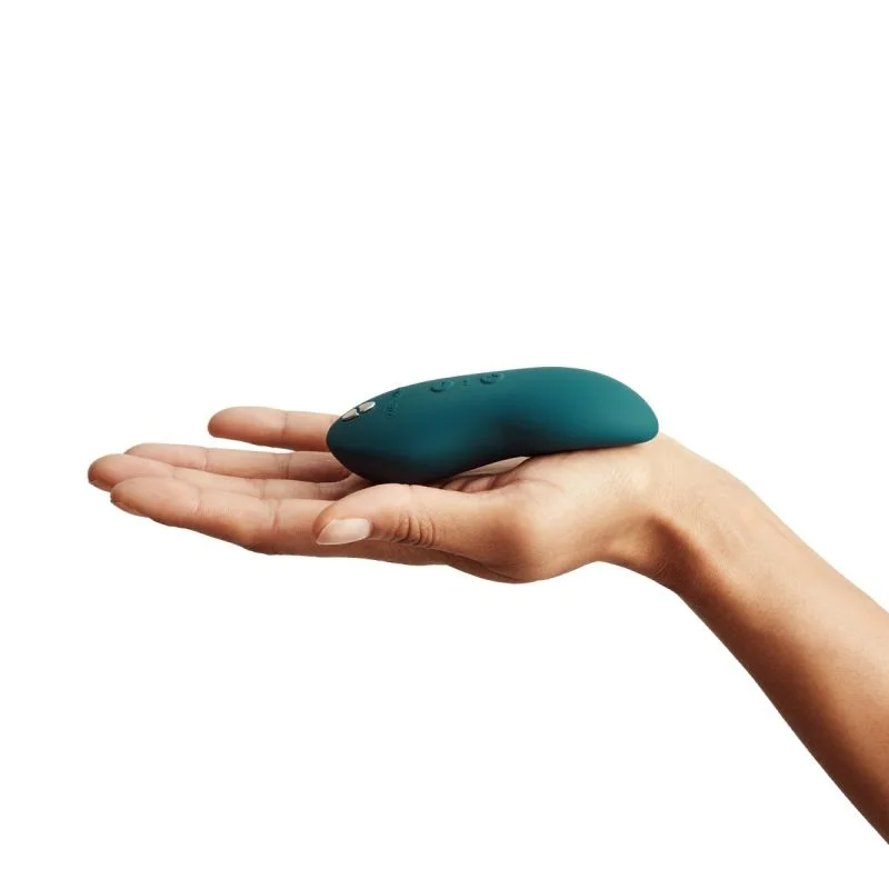 A teal vibrating massager rests on an open palm.