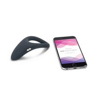 A dark grey vibrating ring and a smartphone displaying the We-Vibe app.