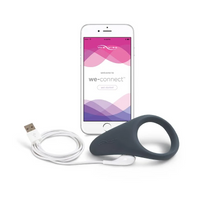 A grey vibrating ring with a white USB cable and a smartphone displaying the We-Vibe app.