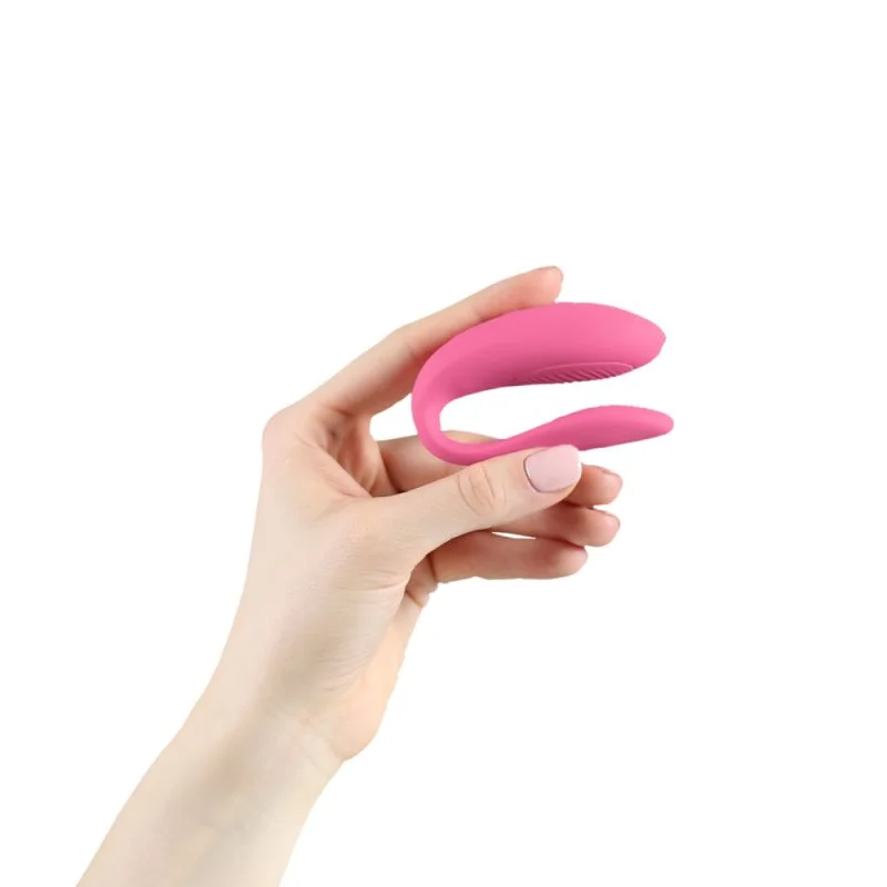 A hand holds a pink app-controlled couples vibrator.