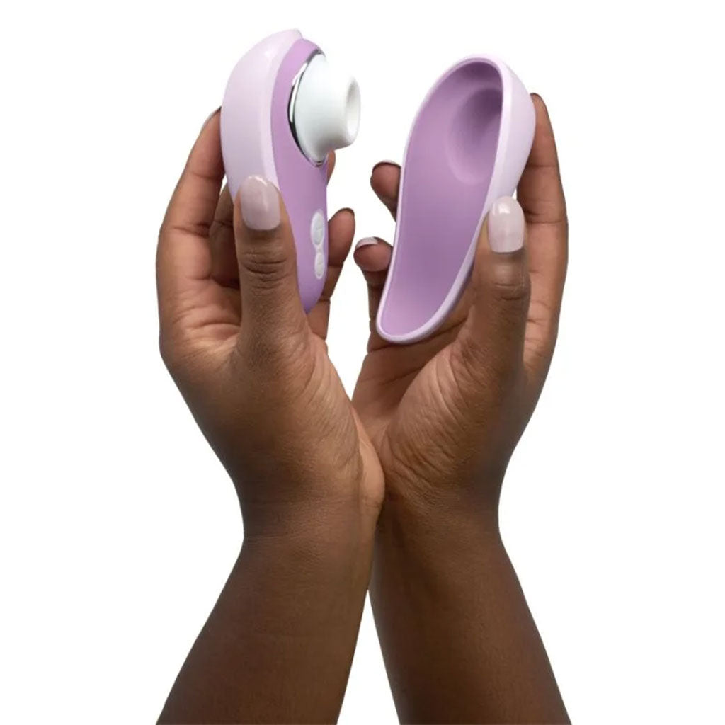 Hands hold a lilac clitoral stimulator and its charging cradle.