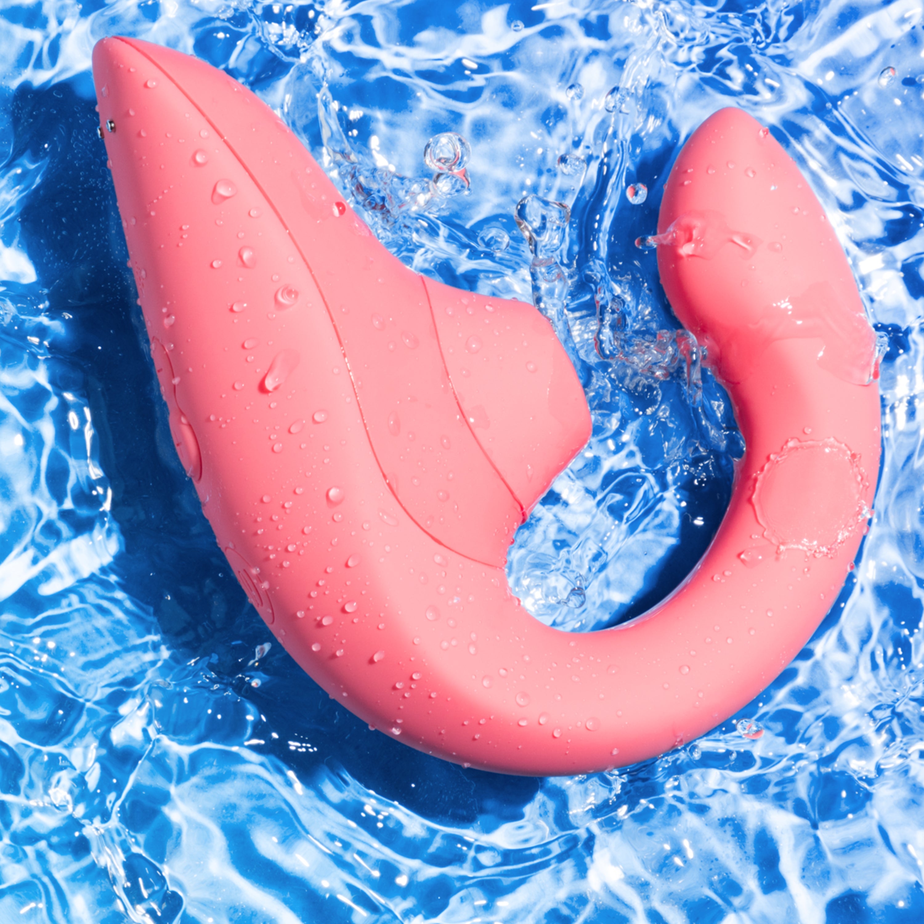 A pink dual stimulation vibrator with water droplets rests in blue water.