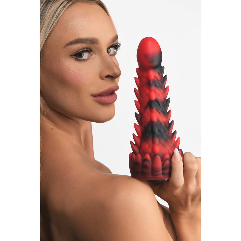 A blonde woman holds a red and black scaly dragon silicone dildo with suction cup base.